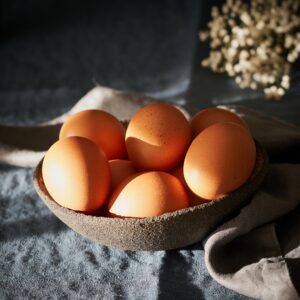 Unusual Easter on dark background. Bowl of brown eggs on dark blue table, flowers.